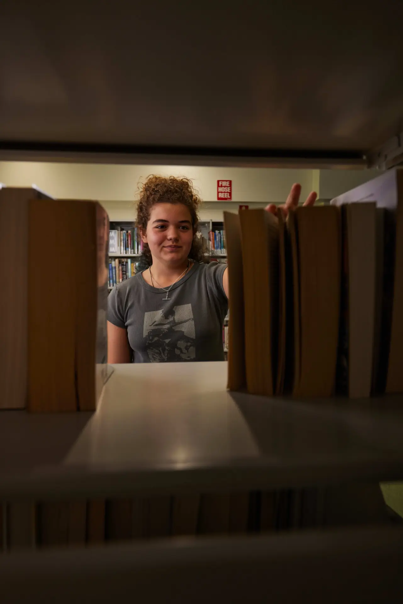View of girl in library between books on bookshelf